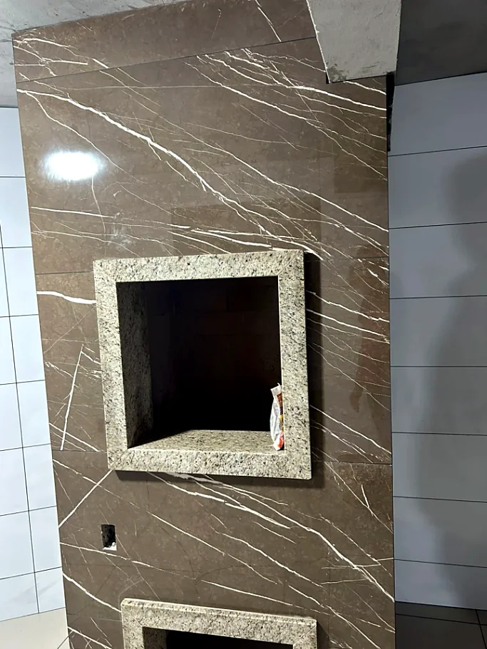 Parede revestida em porcelanato marrom com veios e nichos com moldura de granito